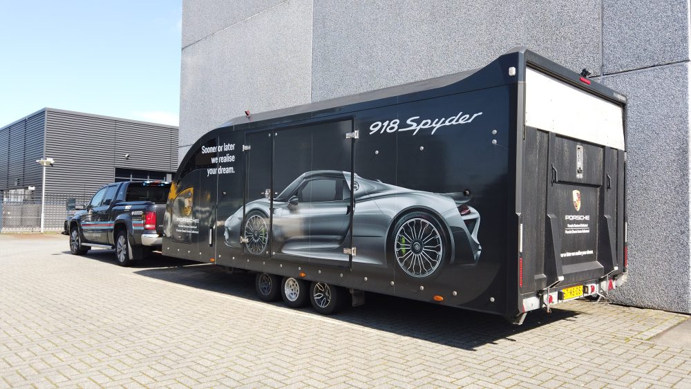 Auto met een speciale aanhanger van Porsche Centrum Gelderland. In deze aanhanger worden auto's vervoerd